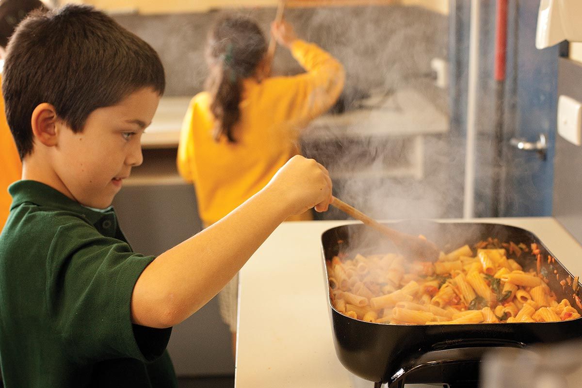 kid cooking pasta with cookbook